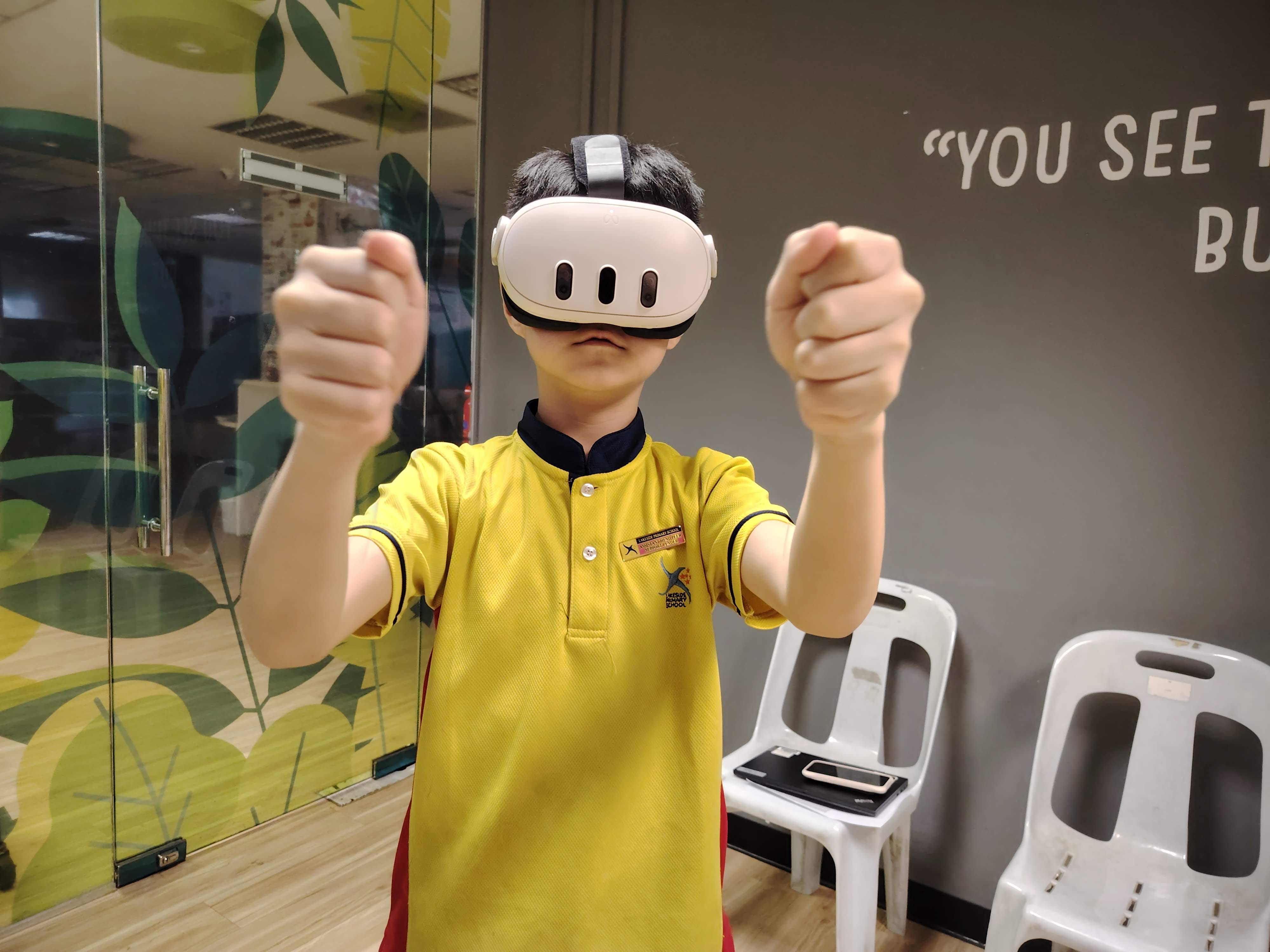 A male student wearing a Meta Quest VR headset stands with both fists raised, fully engaged in the mixed reality experience during the workshop.